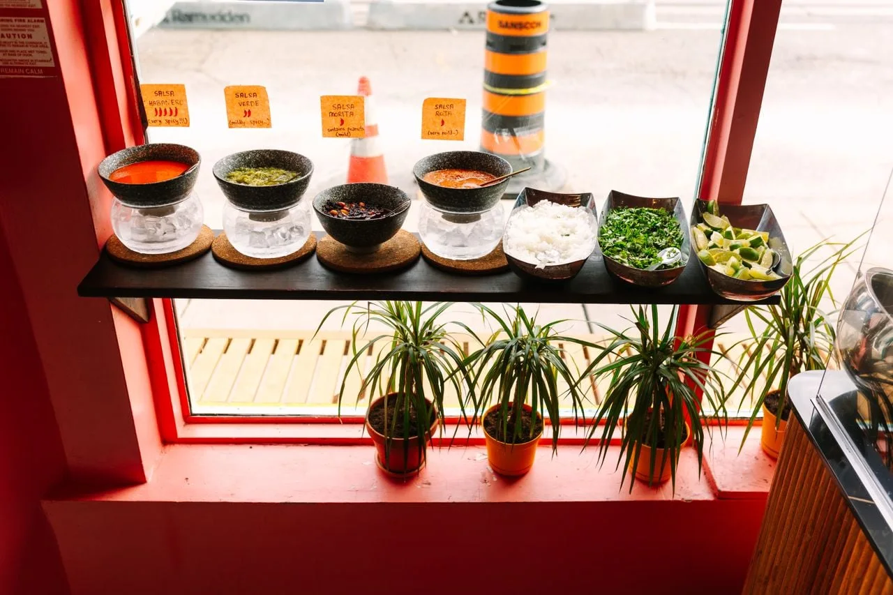 A row of sauces beside the window at Holi Taco