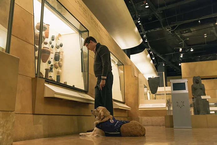 A visitor with a service dog beside museum displays at the ROM