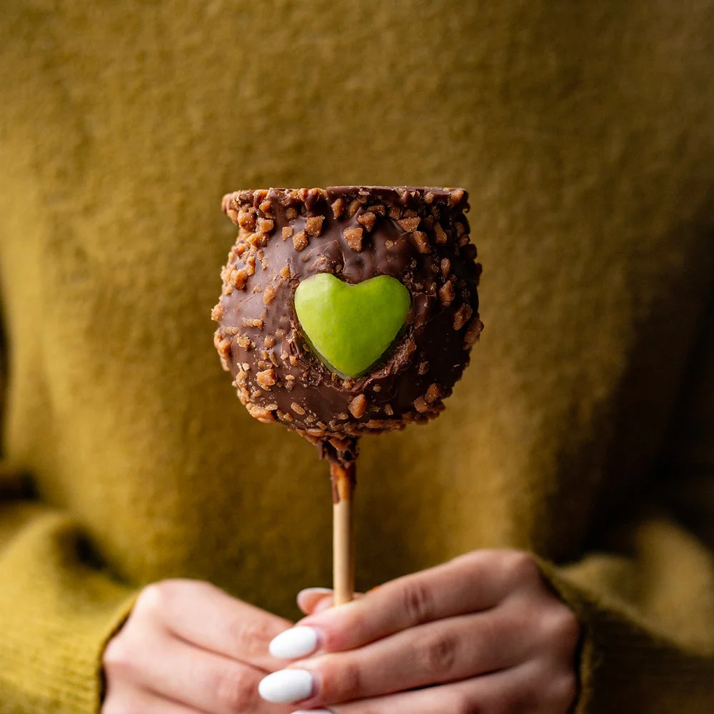 Hands holding a decorated chocolate and caramel apple