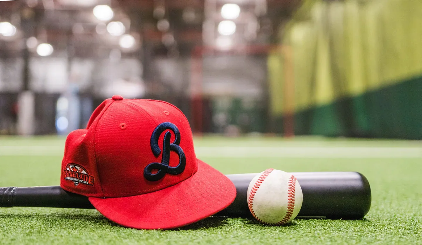 A red Baseline Sports cap, baseball and bat rest on green turf
