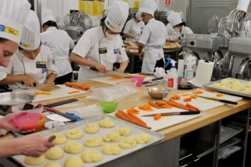 Students in chef uniforms practise food preparation in a George Brown teaching kitchen