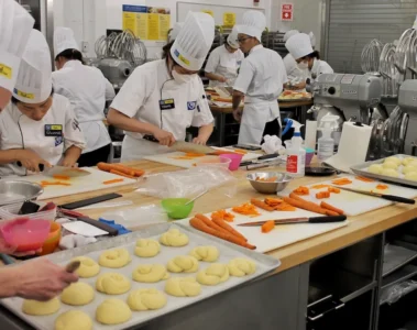 Students in chef uniforms practise food preparation in a George Brown teaching kitchen