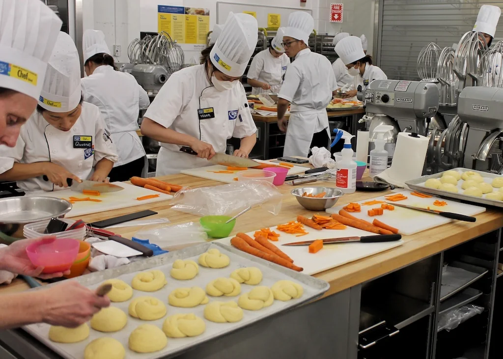 Students in chef uniforms practise food preparation in a George Brown teaching kitchen