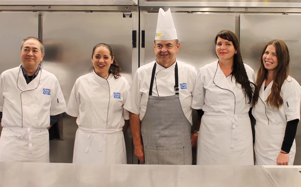 John Higgins and four participants stand together in chef coats in a George Brown kitchen