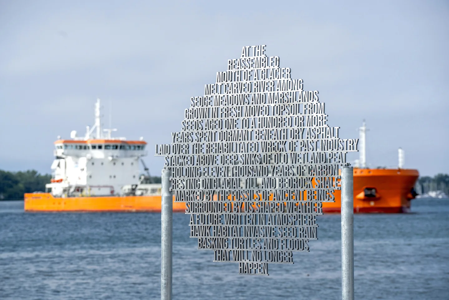 Reflective metal letters form an outdoor sculpture beside the water