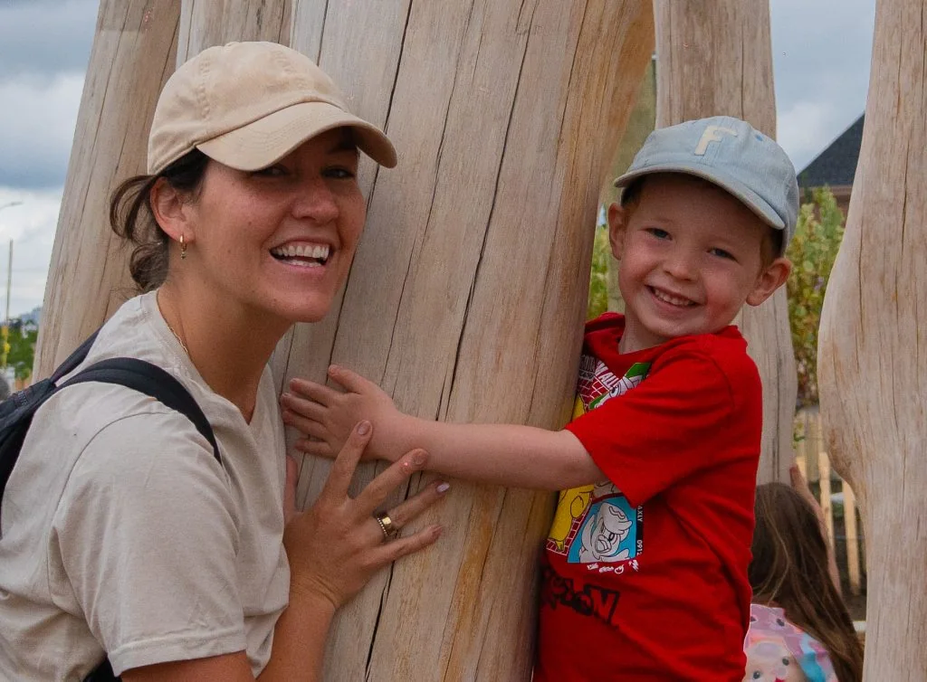 A woman and child explore a wooden beaver play structure