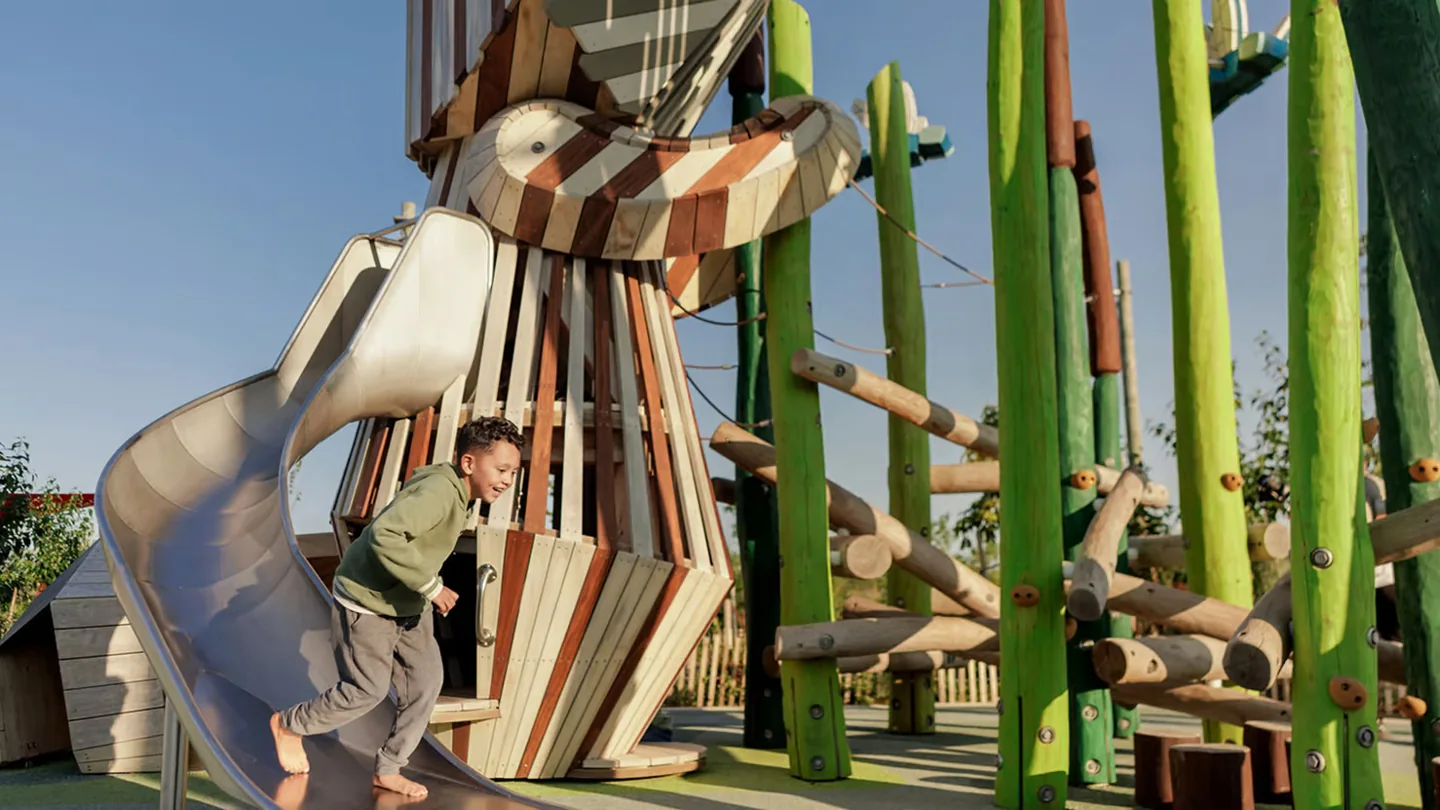 A child beside the large wooden raccoon playground