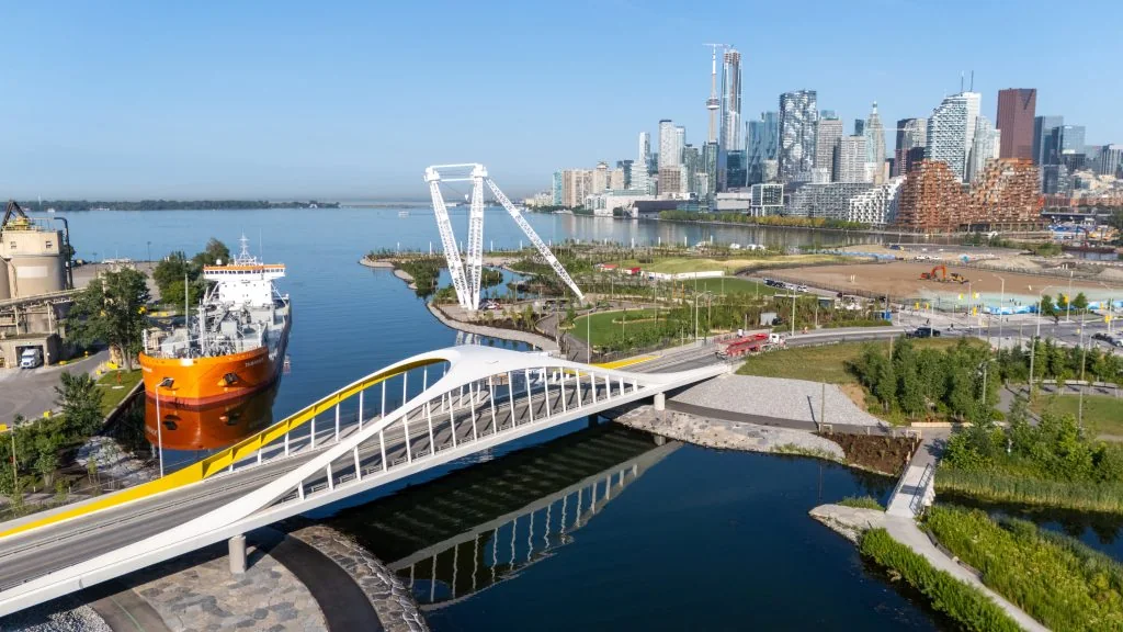 An aerial view of a white pedestrian bridge, the Atlas Crane and Toronto Harbour