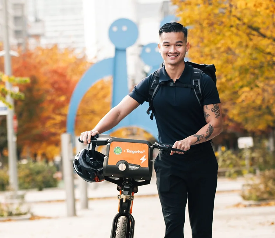 A smiling rider with a backpack stands beside a Bike Share bicycle