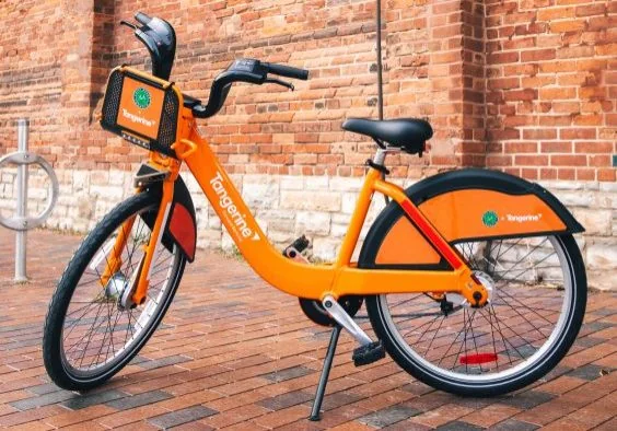 An orange classic Bike Share Toronto bicycle beside a brick wall