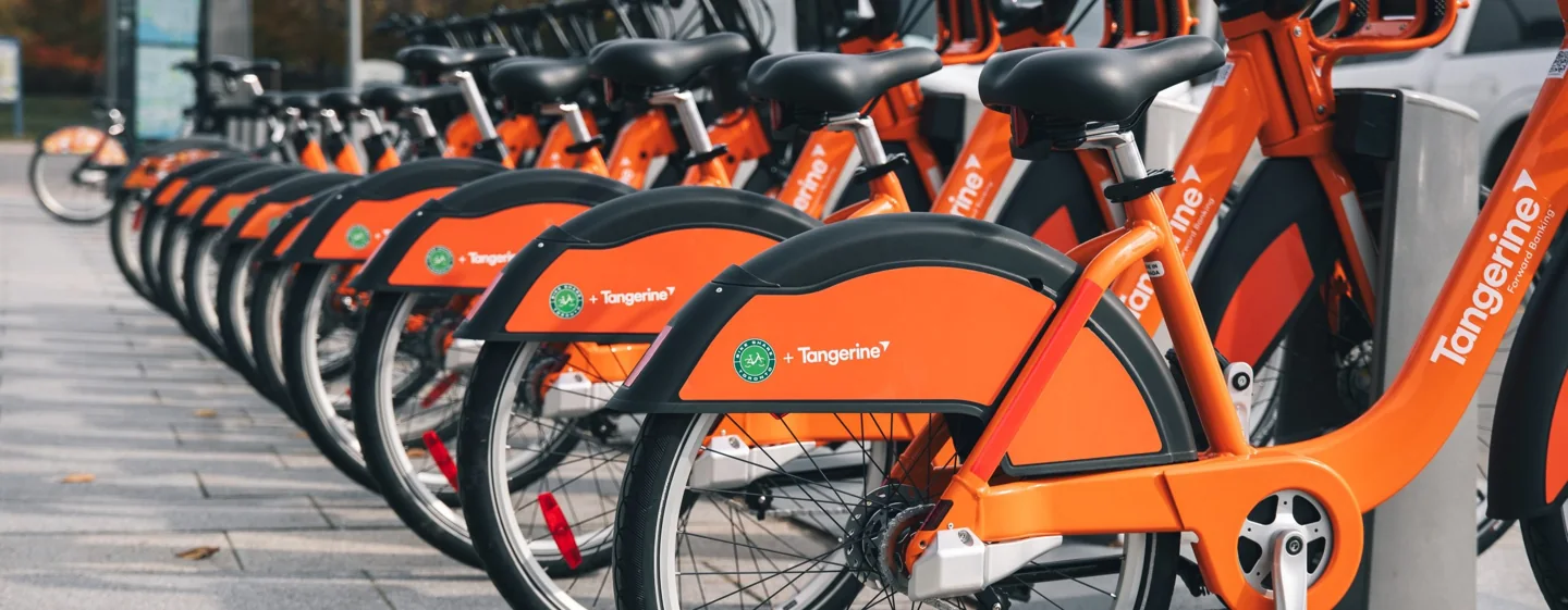 Orange Bike Share bicycles lined up in docks on a city sidewalk