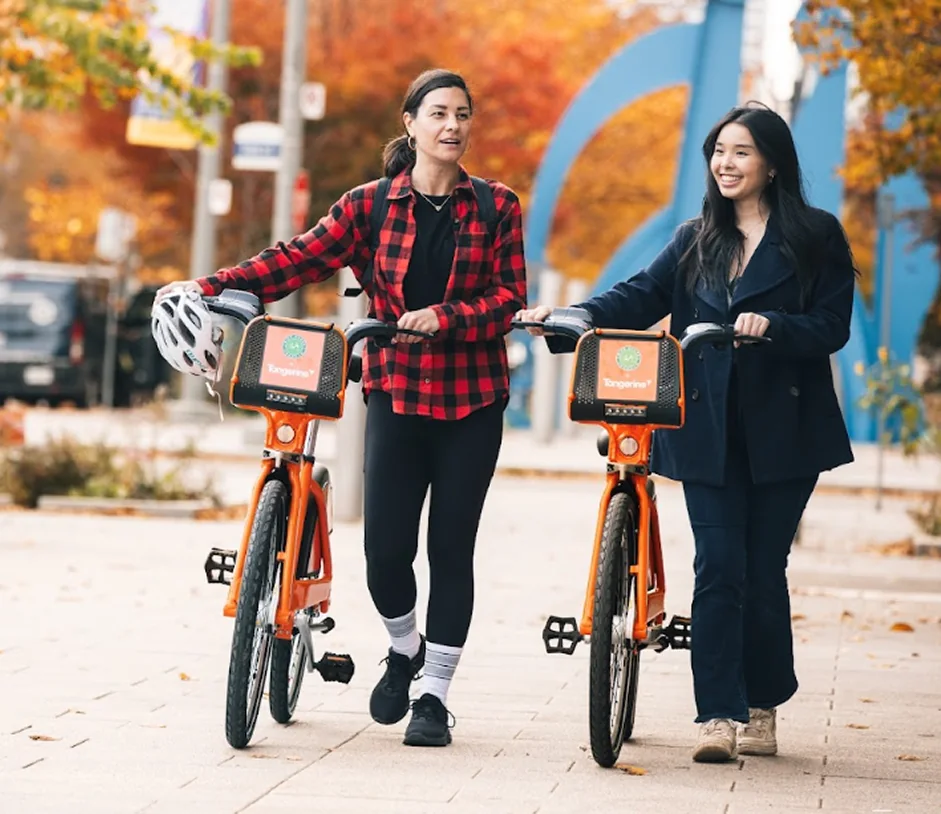 Two women walk beside orange Bike Share Toronto bikes