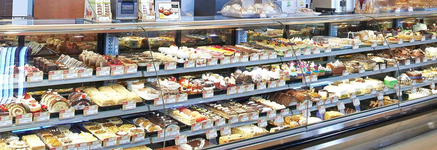 A long Yummy Market refrigerated display filled with cakes and pastries
