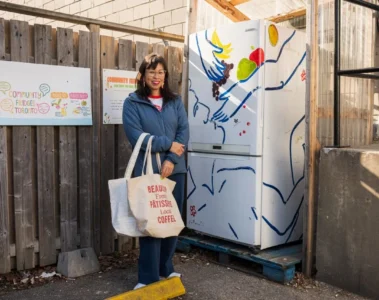 Pay Chen stands with shopping bags beside the painted community fridge on Adelaide Street West
