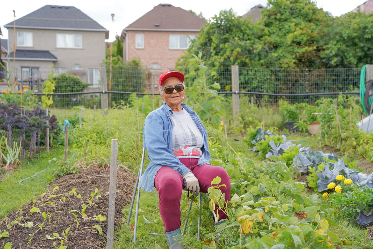 A woman in a red cap sits beside crops in a community garden