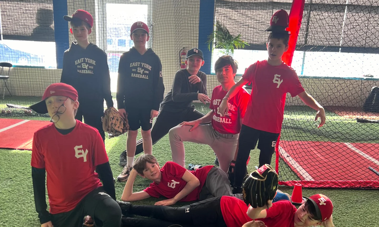 Young baseball players gather inside a netted training area