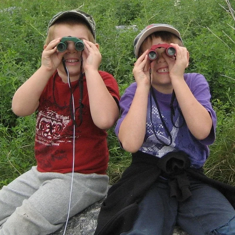 Two children look through binoculars outdoors