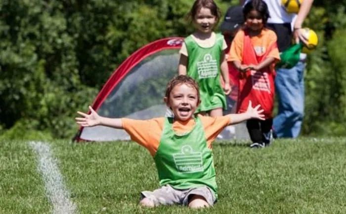 Children play on grass beside small soccer goals