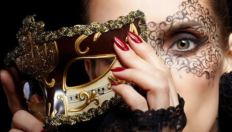 A woman holds a decorative masquerade mask beside painted eye makeup