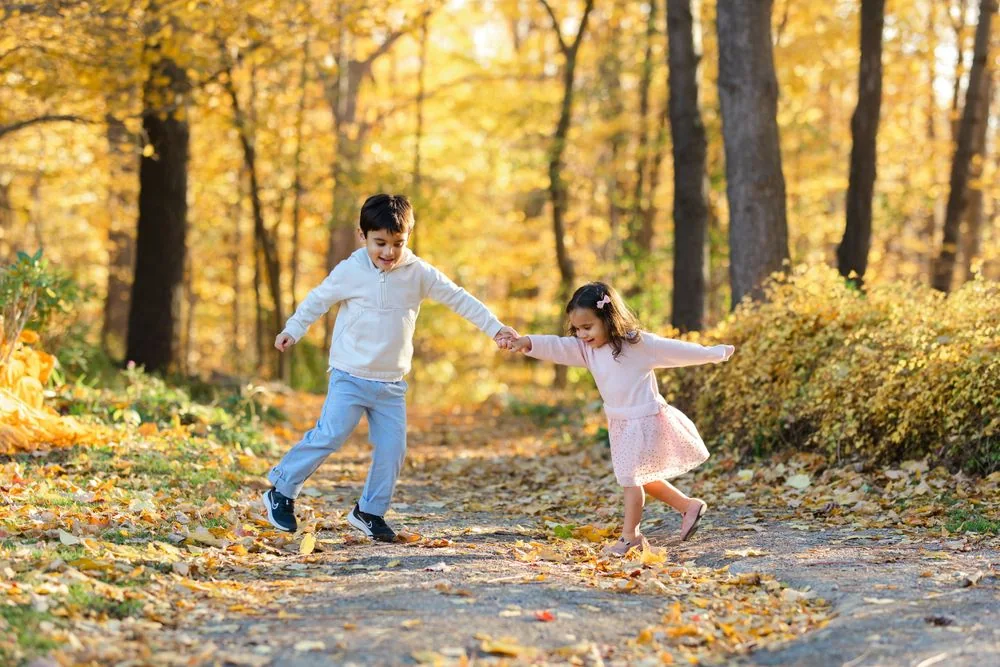 Two people playing on a leaf-covered path at Humber Arboretum