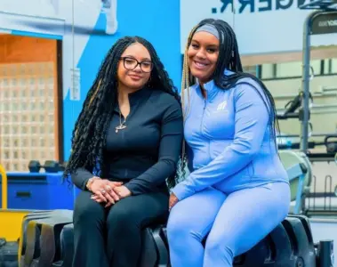 TMU students Cami Rabia and Abbygail Baker-Douglas sitting together in a workout room