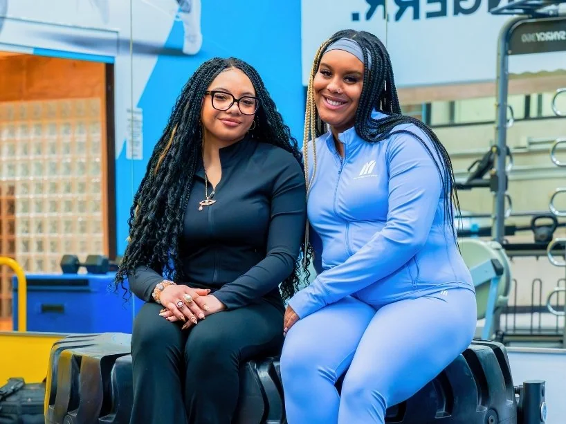 TMU students Cami Rabia and Abbygail Baker-Douglas sitting together in a workout room