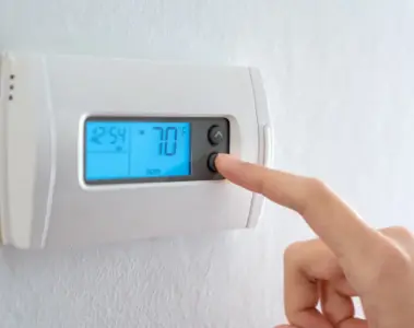 A hand adjusts a wall thermostat.