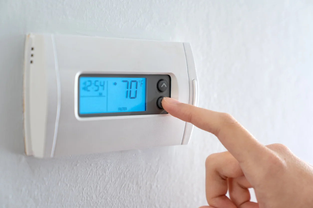 A hand adjusts a wall thermostat.
