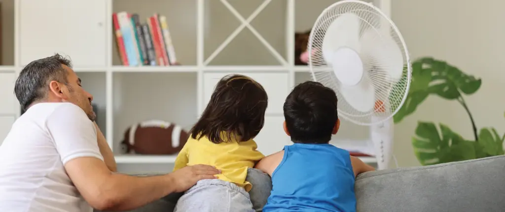 A family sits near a fan on a warm day.
