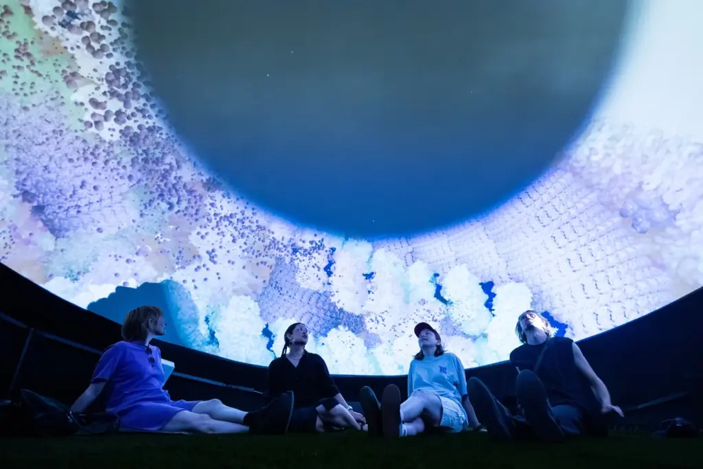 Visitors seated beneath a large projected digital artwork by SJ Okemow