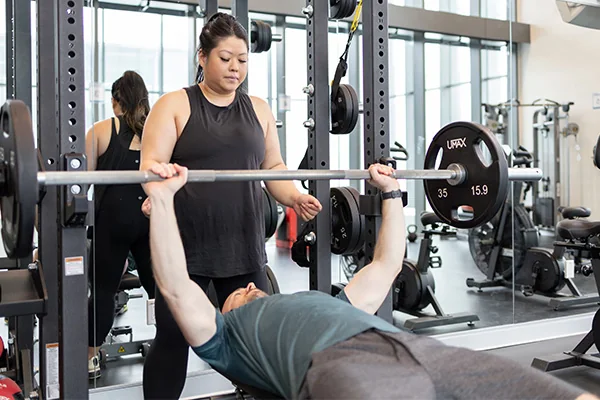 A trainer spotting a person doing a bench press in the gym.