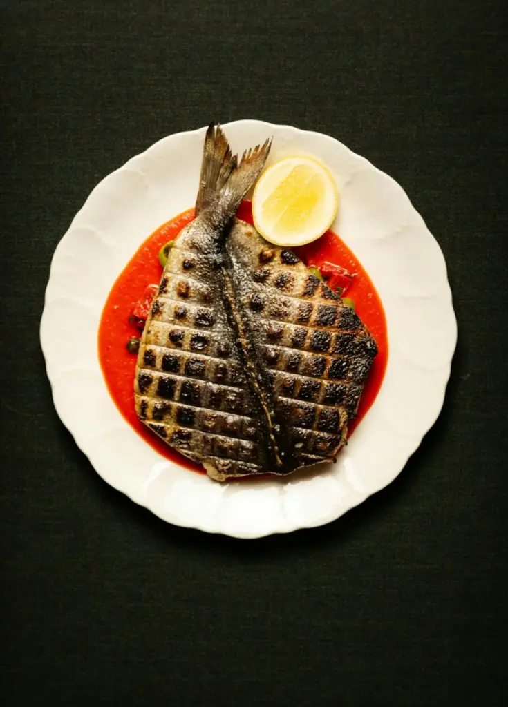 A grilled whole fish on a white plate at Alder