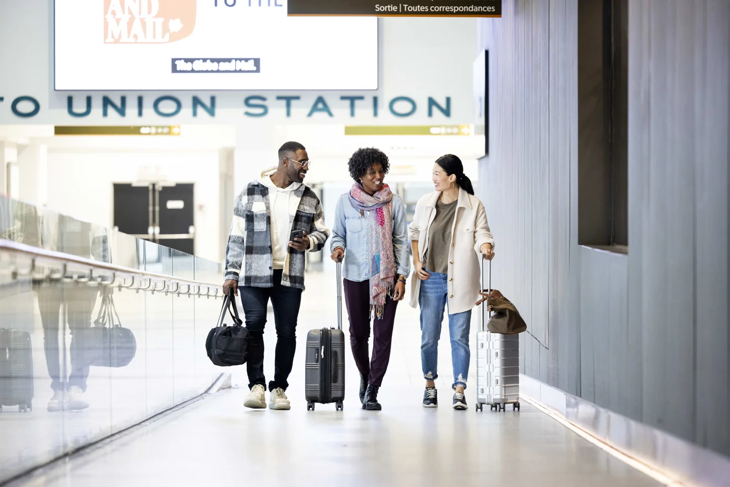 Three travellers with suitcases walk towards the UP Express terminal at Union Station
