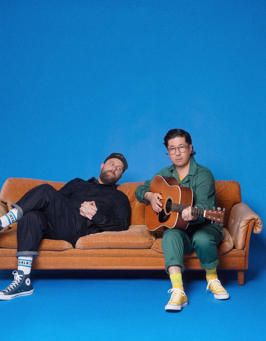 Choir! Choir! Choir! directors Daveed Goldman and Nobu Adilman sit on a sofa with a guitar