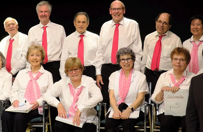 Choralairs members in white tops and pink scarves or ties stand and sit together