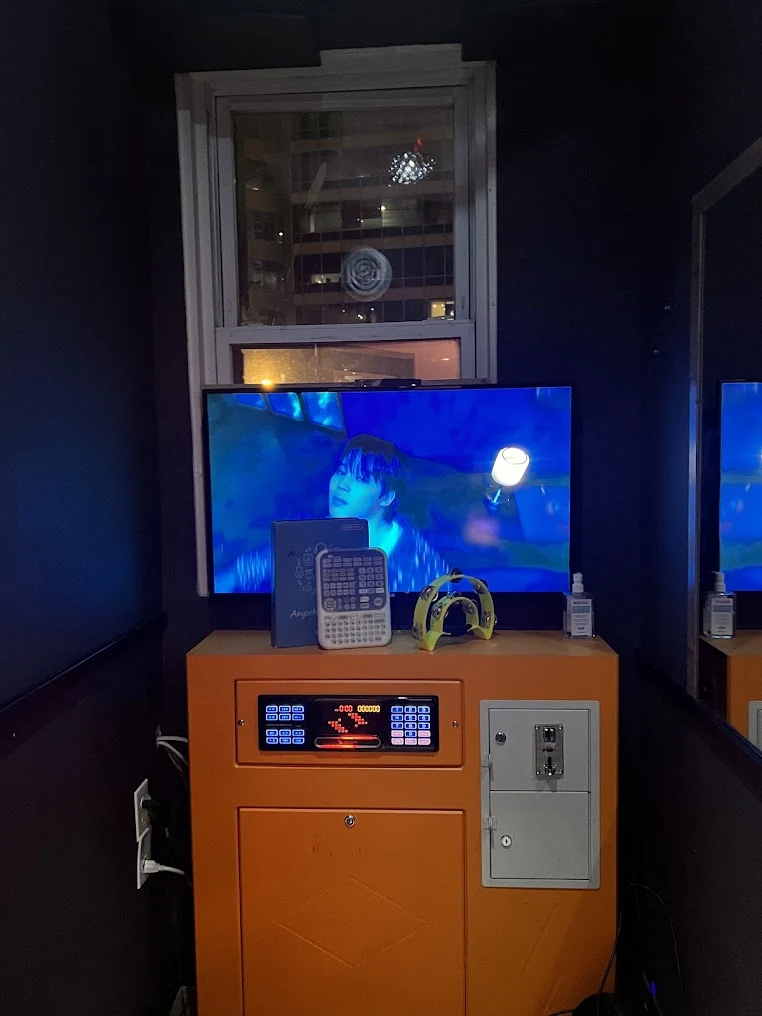 A screen, song controller and orange karaoke machine inside an Echo Coin Karaoke booth