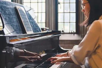A woman plays a grand piano beside a sunlit window at Hart House