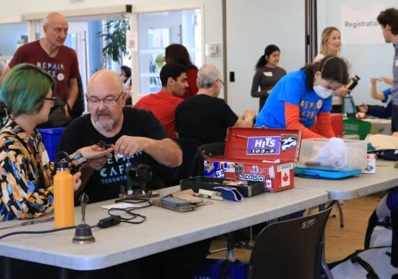 Visitors and volunteer fixers sit together around repair tables