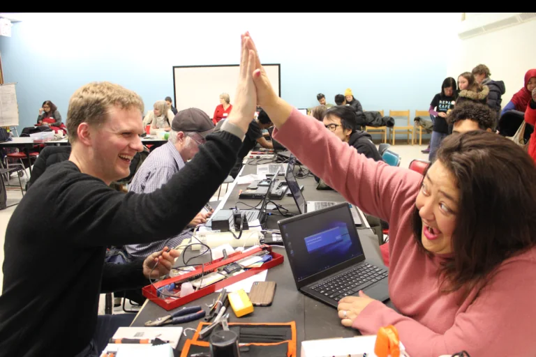 A fixer and visitor high-five across a repair table
