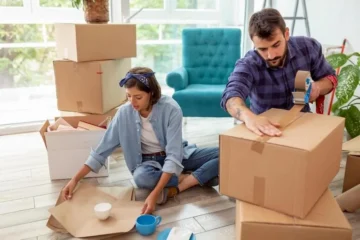 A woman and man pack household belongings into cardboard boxes