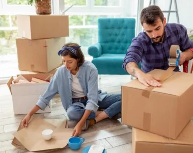 A woman and man pack household belongings into cardboard boxes