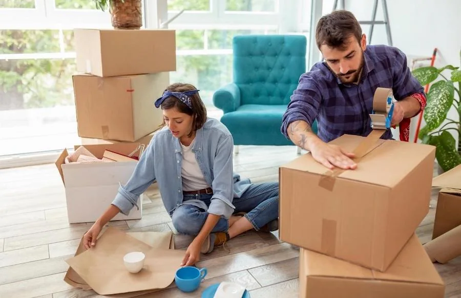 A woman and man pack household belongings into cardboard boxes