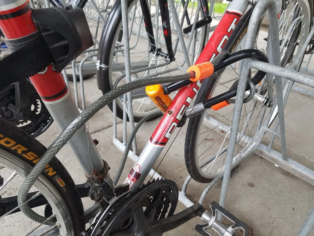 A bicycle secured to a rack with a U-lock and a cable through its wheels