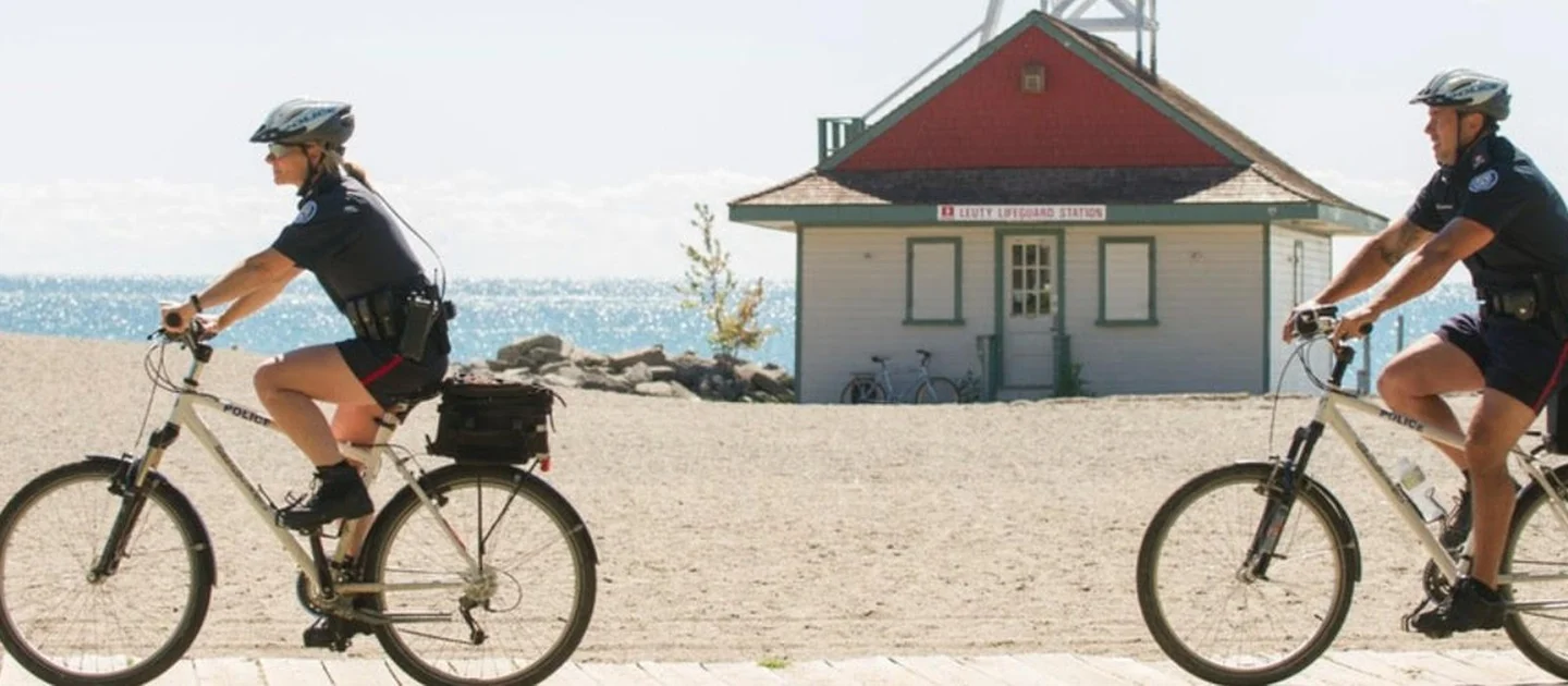 Two Toronto police officers ride bicycles past Leuty Lifeguard Station
