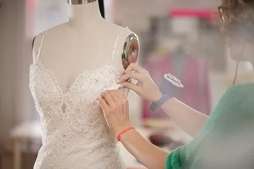 Hands check the fit of a lace dress on a dress form