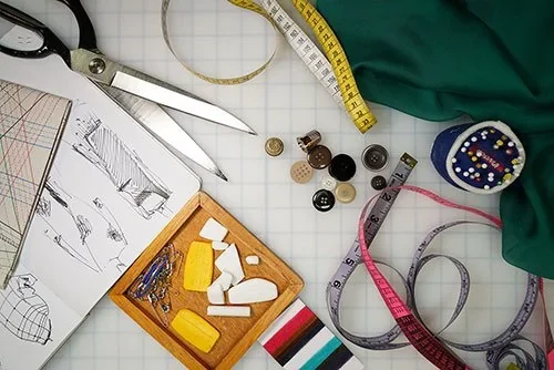 Pattern sketches, sewing scissors, buttons and measuring tape on a work table