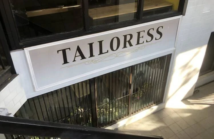 Stairs lead down to the Tailoress window and sign