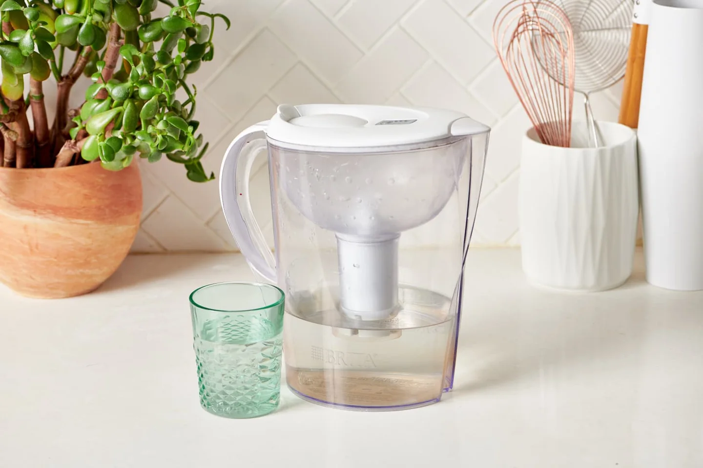 A covered water-filter pitcher and a glass on a kitchen counter