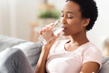 A woman drinks a glass of water at home