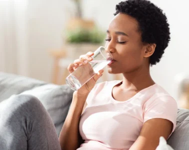 A woman drinks a glass of water at home